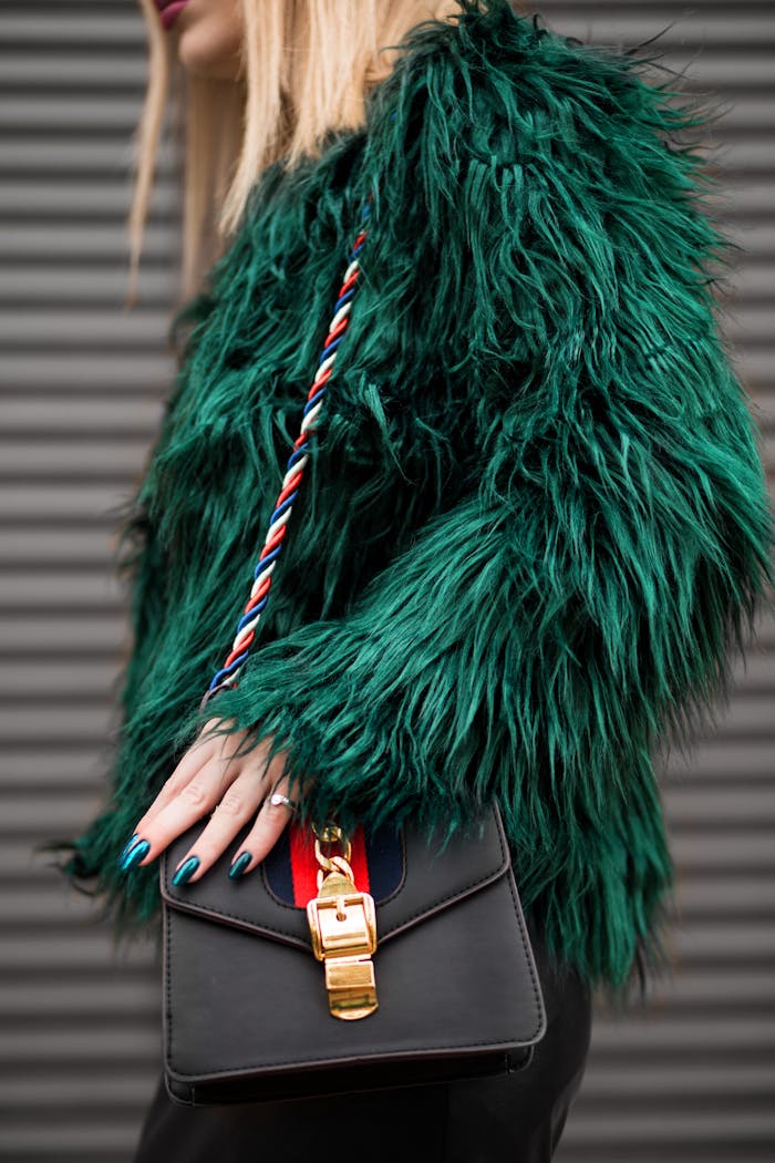 Stylish woman in a green faux fur jacket holding a fashionable handbag outdoors.